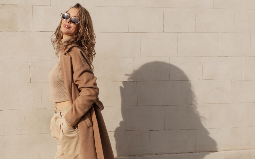woman wearing sunglasses and trench coat in front of wall