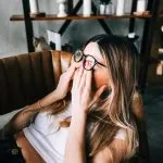 Woman in her 40s sitting in a chair rubbing her eyes, illustrating fatigue, brain fog, and low energy linked to hormones, B12 deficiency, or perimenopause - solutions offered at Greenwich Medical Spa.