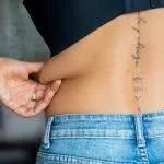 Close-up of a woman pinching stubborn belly fat, illustrating the difference between CoolSculpting vs liposuction for targeted fat reduction and body contouring.