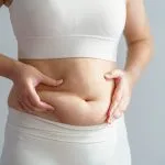 Close-up of a midlife woman pinching abdominal fat, illustrating hormones and belly fat, menopause belly fat, and how metabolism and hormones affect midlife weight gain. Solutions offered at Greenwich Medical Spa.