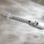 Syringe drawing liquid from a small vial on a marble surface, illustrating peptide safety, FDA-approved peptide treatments, peptide risks, and research peptides meaning for patients at Greenwich Medical Spa.