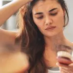 Woman examining hair shedding in a brush, illustrating hair loss after 40, menopause hair loss, and hormonal hair thinning in women. Featured image for Greenwich Medical Spa's guide to the connection between perimenopause, estrogen changes, and female hair thinning after 40.